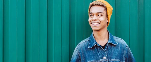 male student standing against wall smiling