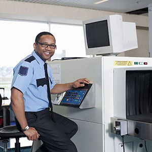 smiling TSA agent sitting at airport luggage scanner